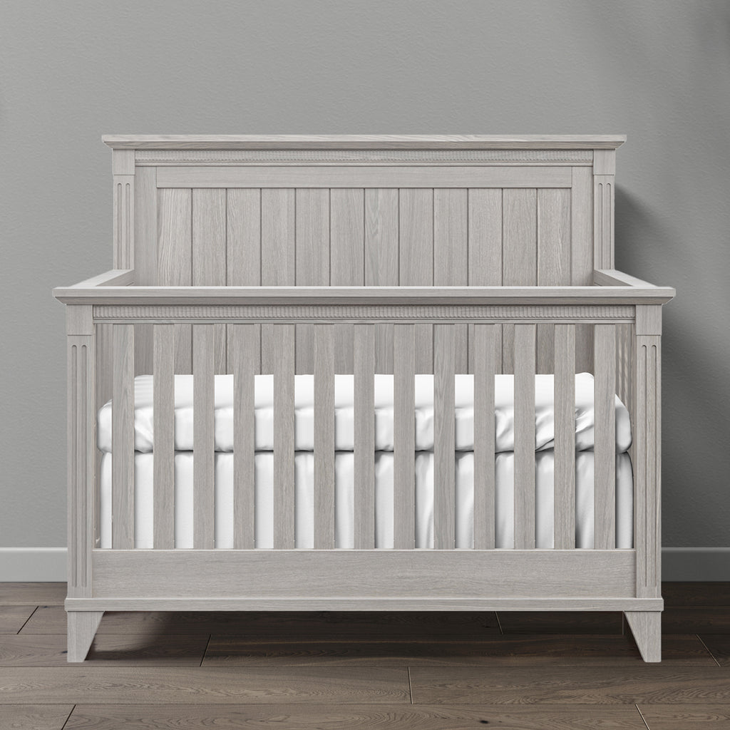 Gray wooden crib with white mattress against a gray wall