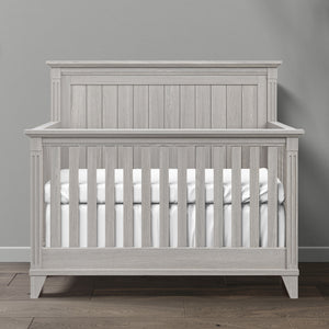 Gray wooden crib with white mattress against a gray wall