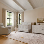Load image into Gallery viewer, Nursery room with white driftwood crib, dresser, and recliner in a well-lit room.
