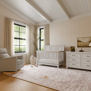 Nursery room with white driftwood crib, dresser, and recliner in a well-lit room.