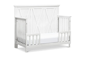 White crib set up as toddler bed with a cross-patterned design on a white background