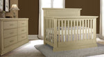 Load image into Gallery viewer, Beige crib and dresser set in a room with brown walls and white curtains.
