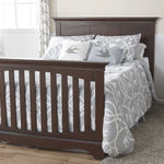 Load image into Gallery viewer, Wooden crib, converted to full size bed, with gray and white patterned bedding in a nursery setting.
