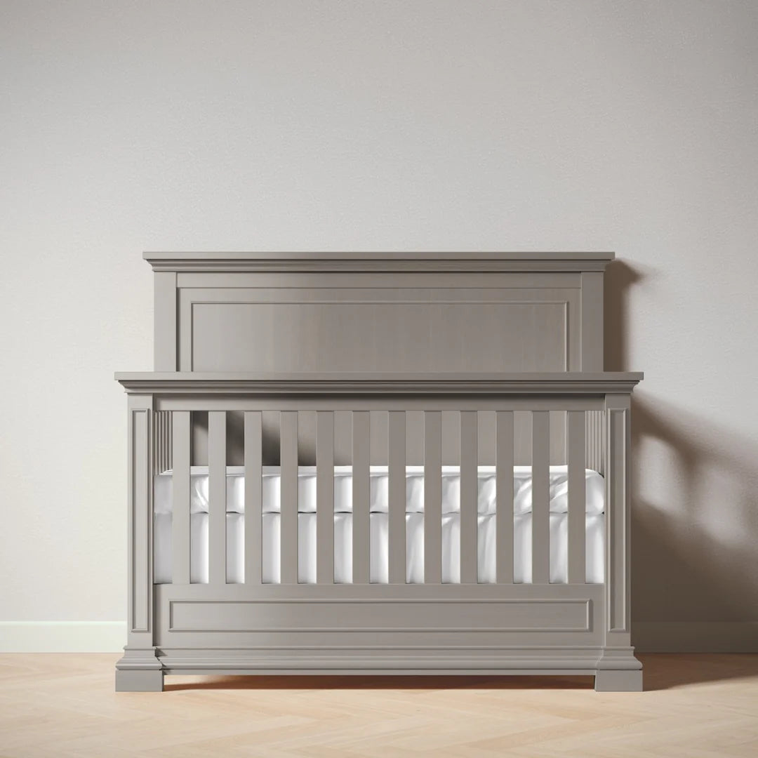 Ash crib with white mattress against a plain wall