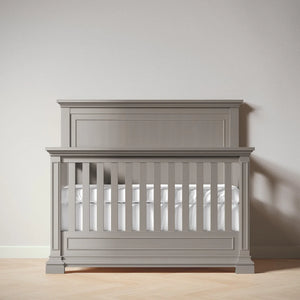 Ash crib with white mattress against a plain wall