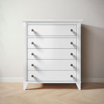Load image into Gallery viewer, White five drawer dresser with bronze knobs on a wooden floor and light gray wall
