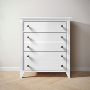 White five drawer dresser with bronze knobs on a wooden floor and light gray wall