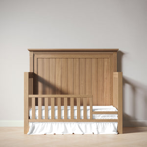 Wooden crib with white mattress against a plain wall