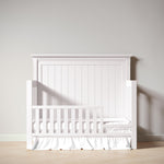 Load image into Gallery viewer, White crib with a wooden headboard against a plain wall
