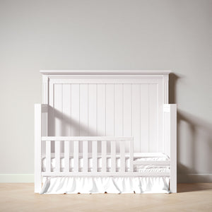 White crib with a wooden headboard against a plain wall