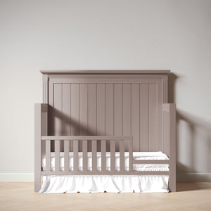 Light wood crib with white mattress against a plain wall