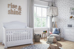 Load image into Gallery viewer, White crib against white wall with rise &amp; shine sign on wall

