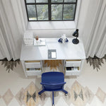Load image into Gallery viewer, A white writing desk with drawers and a blue rolling office chair in front, styled in a bright room with a window, curtains, patterned rug, and desk accessories.

