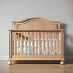 Load image into Gallery viewer, Wooden crib with white bedding on a wooden floor against a gray wall
