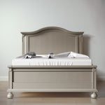 Load image into Gallery viewer, A light gray wooden bed frame with an arched headboard and matching footboard, styled with a white mattress and gray and white pillows, set against a neutral gray wall and light wood floor.
