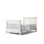 Load image into Gallery viewer, White wooden  crib converted to full bed, shown on a white background with white bedding.
