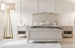 Load image into Gallery viewer, A classic white wooden bed frame with a curved headboard and footboard, styled in a bright bedroom with matching nightstands, a floor lamp, and a white rug.
