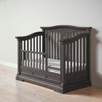 Load image into Gallery viewer, Dark wood crib, converted to toddler bed, with mattress on a light wooden floor and white wall background
