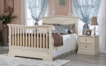 Load image into Gallery viewer, A cream-colored wooden convertible crib (converted to a full bed) with blue patterned curtains, a matching nightstand, and neutral bedding.

