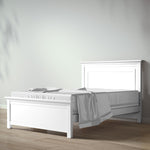 Load image into Gallery viewer, A white wooden bed frame with a matching headboard and footboard, styled with white bedding and a light gray throw blanket, set against a minimalist light gray wall and light wood floor.
