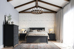 Load image into Gallery viewer, A styled bedroom interior featuring a dark gray wooden bed frame, matching nightstands, a tall dark dresser, and a patterned wallpaper on the back wall. The room has a high vaulted ceiling with exposed dark wood beams, a hanging ring chandelier, and sheer white curtains by a bright window.

