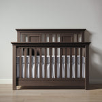 Load image into Gallery viewer, Wooden crib with white bedding against a plain wall
