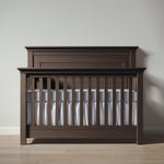 Load image into Gallery viewer, Wooden crib with white bedding against a plain wall
