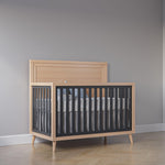 Load image into Gallery viewer, Wooden crib with black side panels against a gray wall
