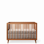 Load image into Gallery viewer, A mid-century modern wooden baby crib with a warm brown finish, featuring vertical slats and tapered legs, shown with a white mattress and gray sheet on a white background.

