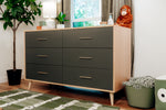 Load image into Gallery viewer, A mid-century modern 6-drawer dresser with dark gray fronts and light wood sides, styled in a nursery or children's room next to a potted plant, window, and toys.
