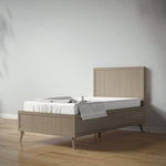 Load image into Gallery viewer, A modern full bed in a light oak finish, styled with a white mattress and a draped white throw blanket, set against a minimalist light gray wall and light wood floor.
