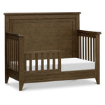 Load image into Gallery viewer, A dark brown wooden toddler bed with a tall panel headboard, slatted side rails, and an attached guard rail, shown with a white mattress on a clean white background.
