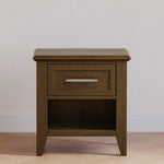 Load image into Gallery viewer, A single-drawer nightstand with an open lower shelf, finished in a medium brown wood grain. It features a silver metal bar handle and is photographed against a neutral, textured off-white wall and light wood floor.
