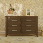 Load image into Gallery viewer, A six-drawer wooden dresser with a medium brown finish and silver metal handles, styled in a bedroom setting against a floral wallpaper background.
